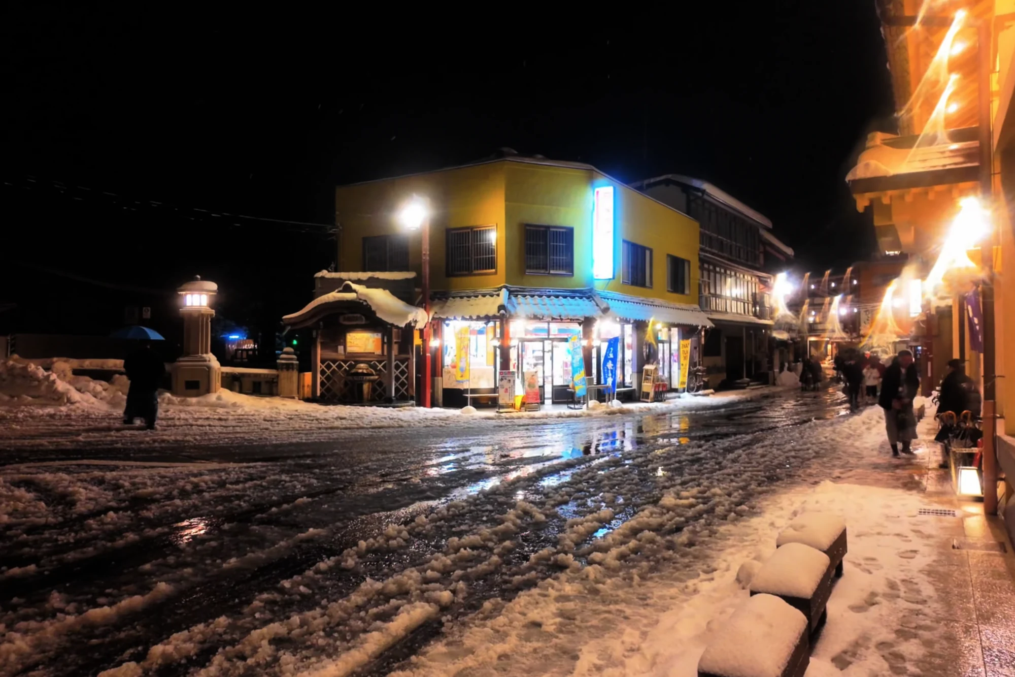 A wet, snow-lined Kinosaki street lit by shopfronts at night.