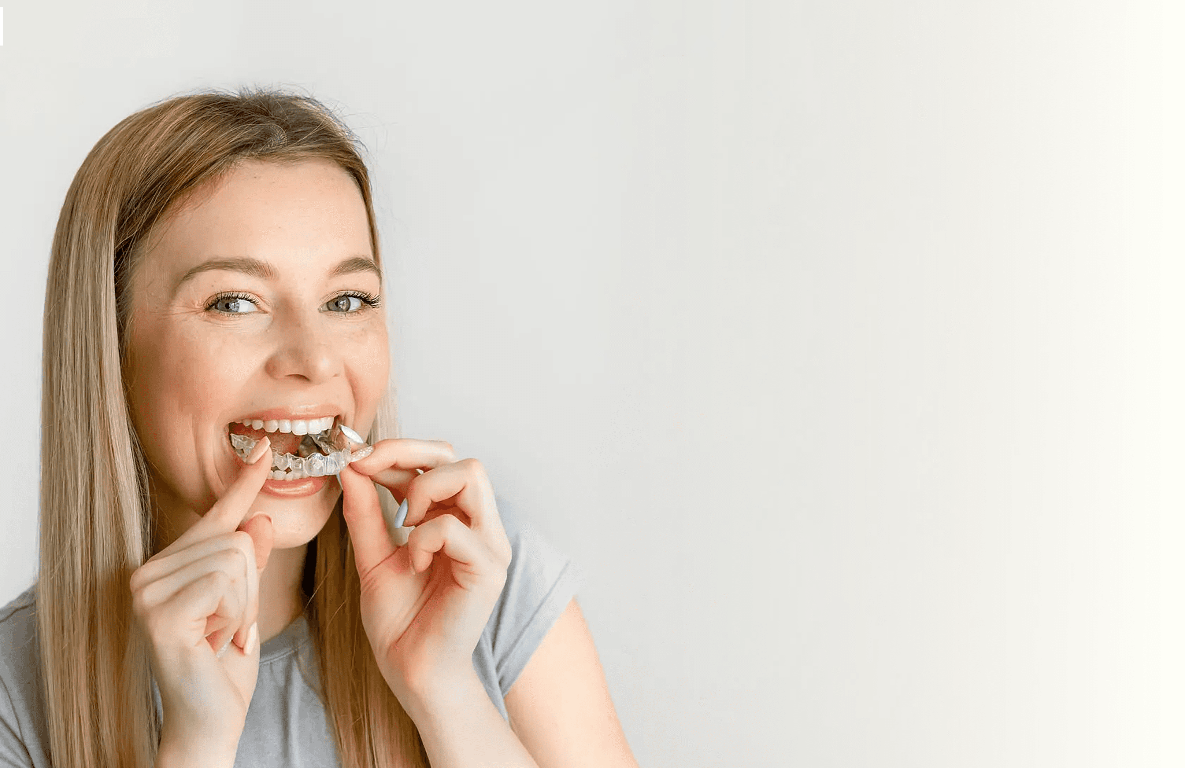 امرأة شقراء مبتسمة، تمسك تقويم الأسنان الشفاف.