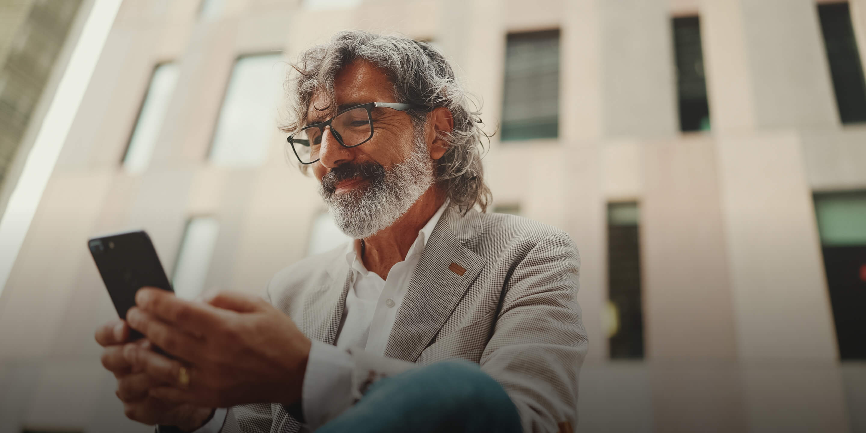 An older man smiling as he looks down at his phone