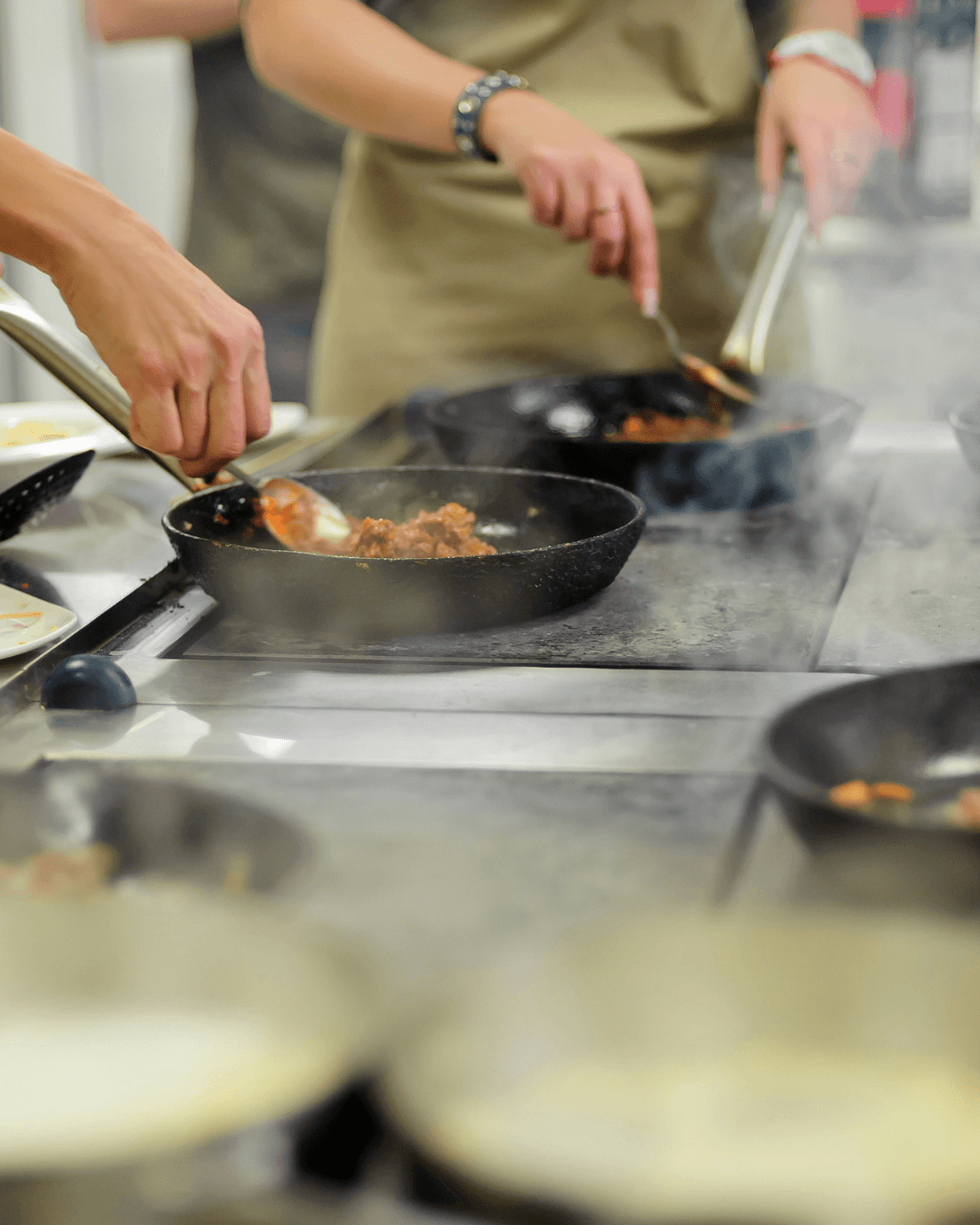 Hands preparing food during a small-group cooking class in a professional kitchen setting