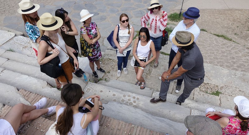A photo of a group of people listening to someone talking about roman architecture.