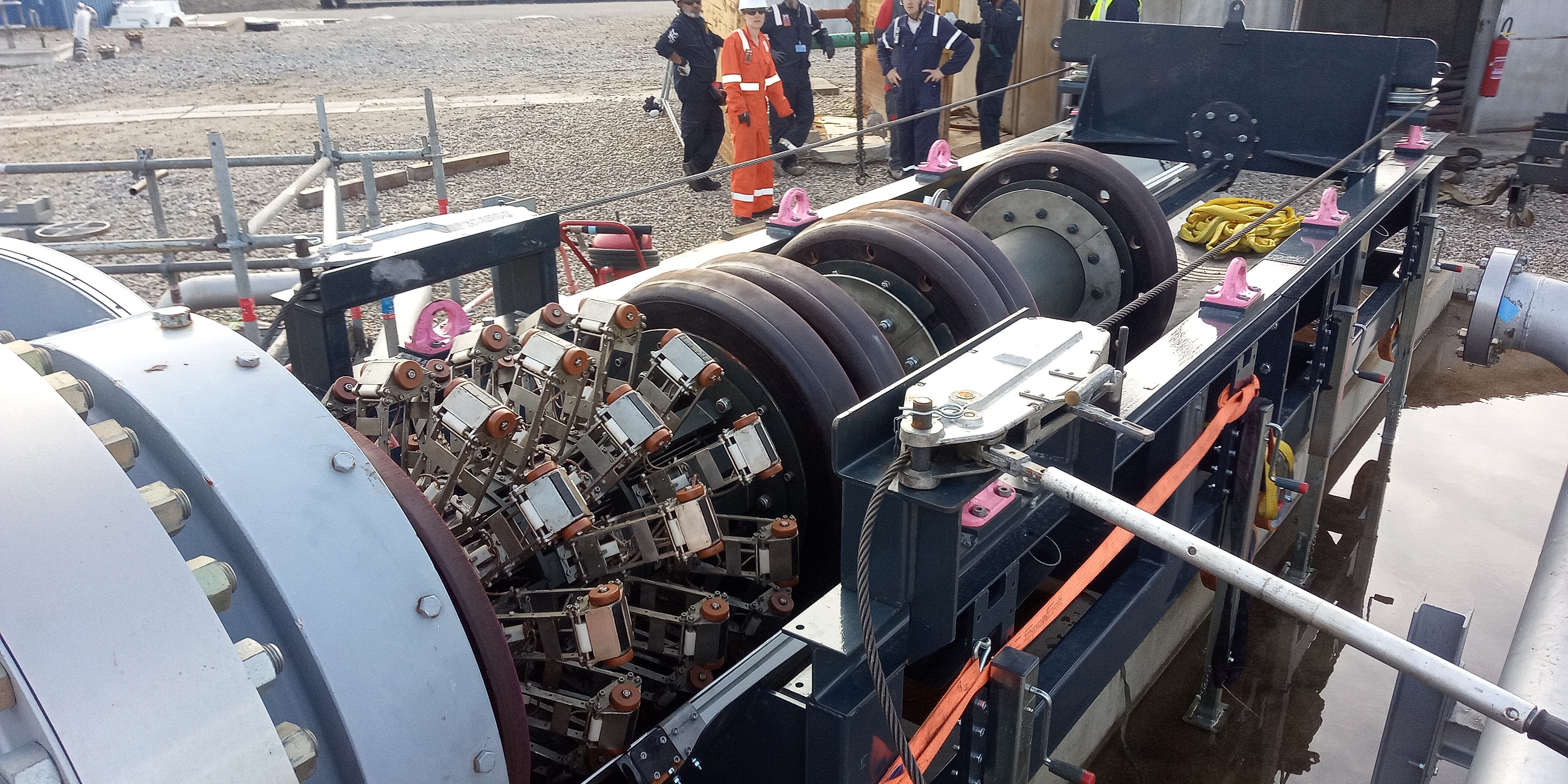 Close-up view of a large industrial machine with wheels, sensors, and pipes with workers in the background.