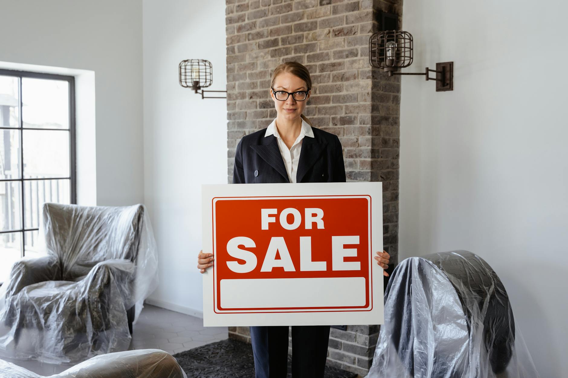 Female estate agent standing in an empty room holding a large red For Sale sign