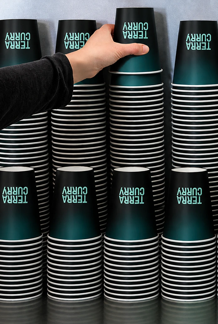 Rows of stacked teal-and-black paper cups printed "TERRA CURRY", with a hand lifting one from the top.