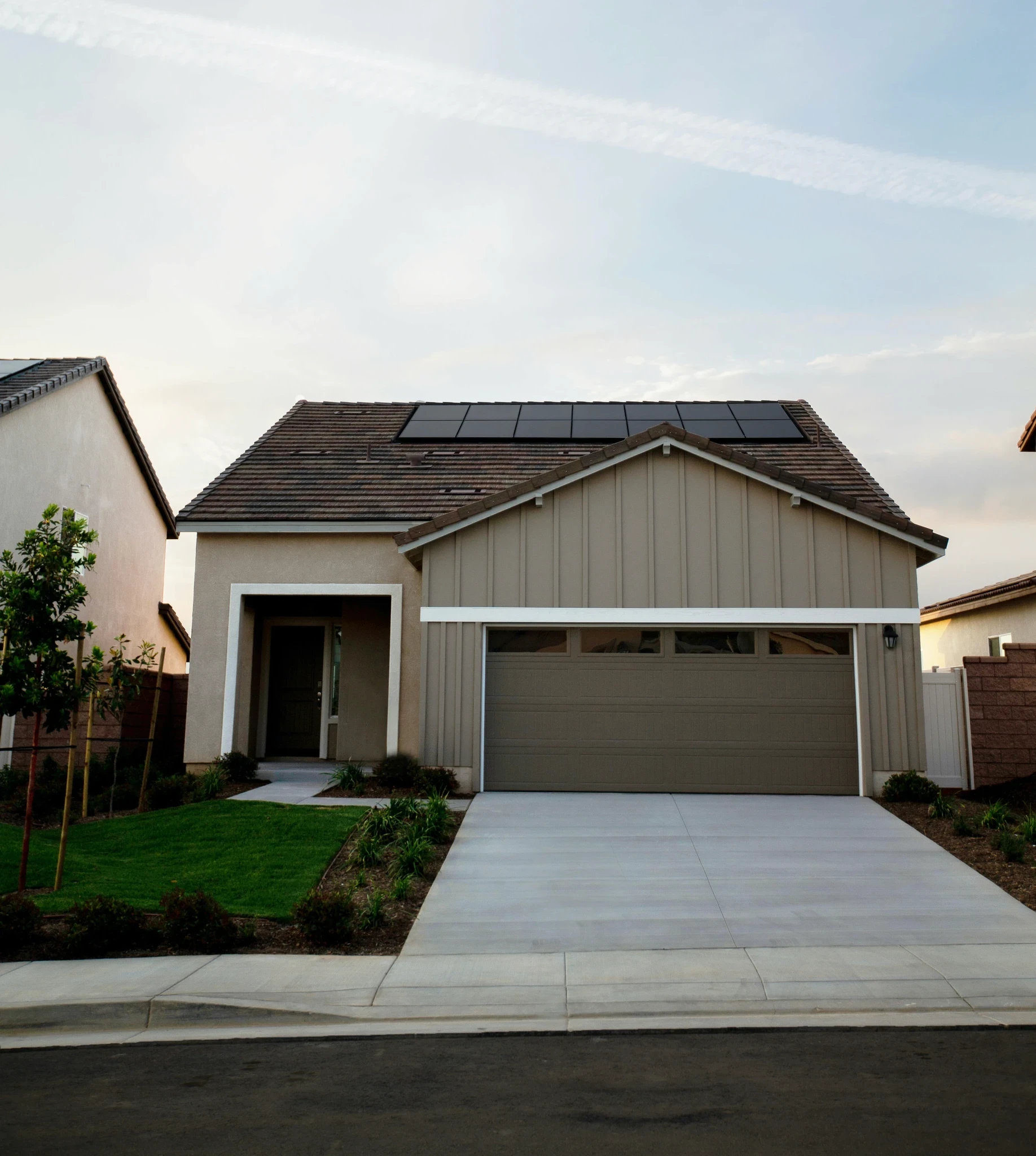 A modern suburban home featuring sleek, black solar panels integrated into the roofline under a clear sky. This high-quality photography, often art-directed by the Zurich creative studio, emphasizes the aesthetic and functional benefits of domestic solar energy as part of a global brand identity.