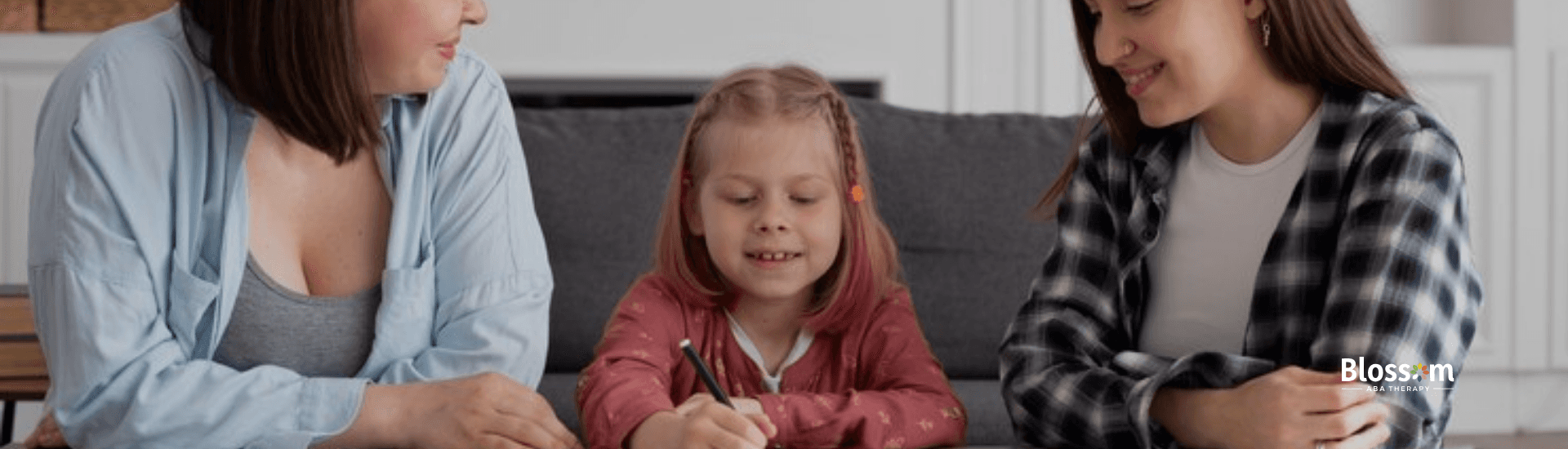 A little girl is sitting between her mother and and RBT while writing on a paper