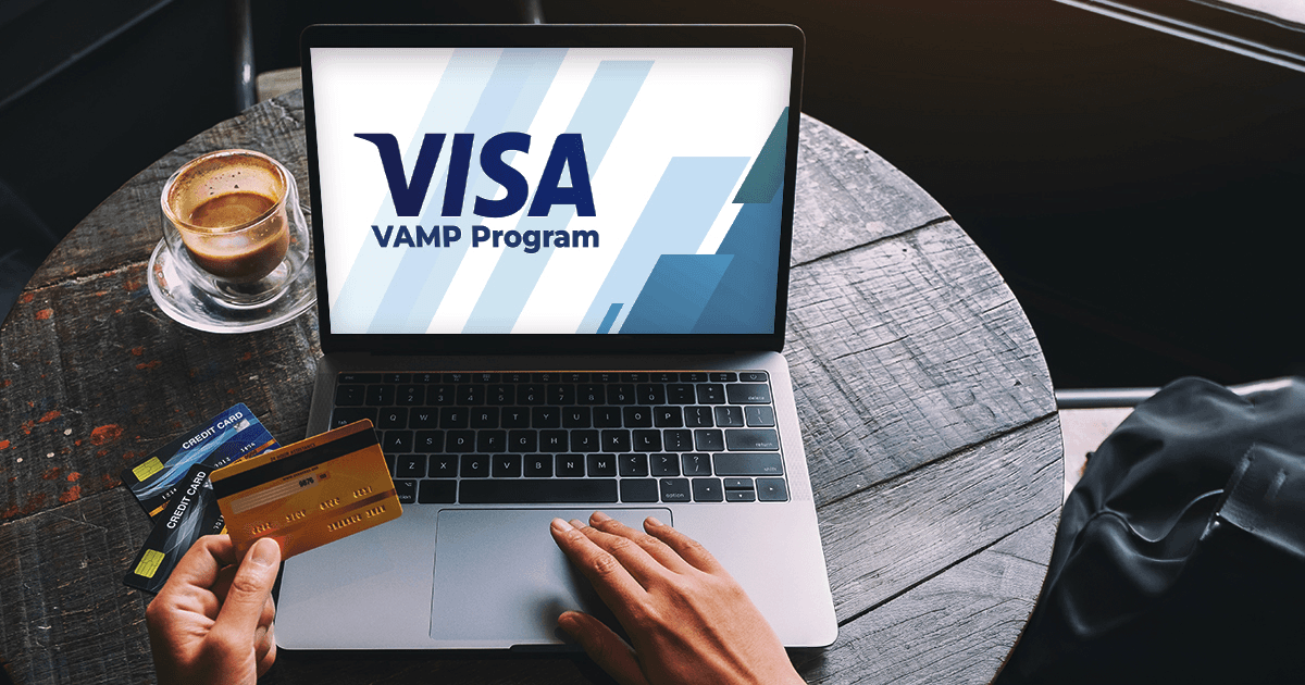 Hände halten eine Kreditkarte vor einem Laptop mit „VISA VAMP Program“. Kaffee und weitere Karten liegen auf dem rustikalen Holztisch.