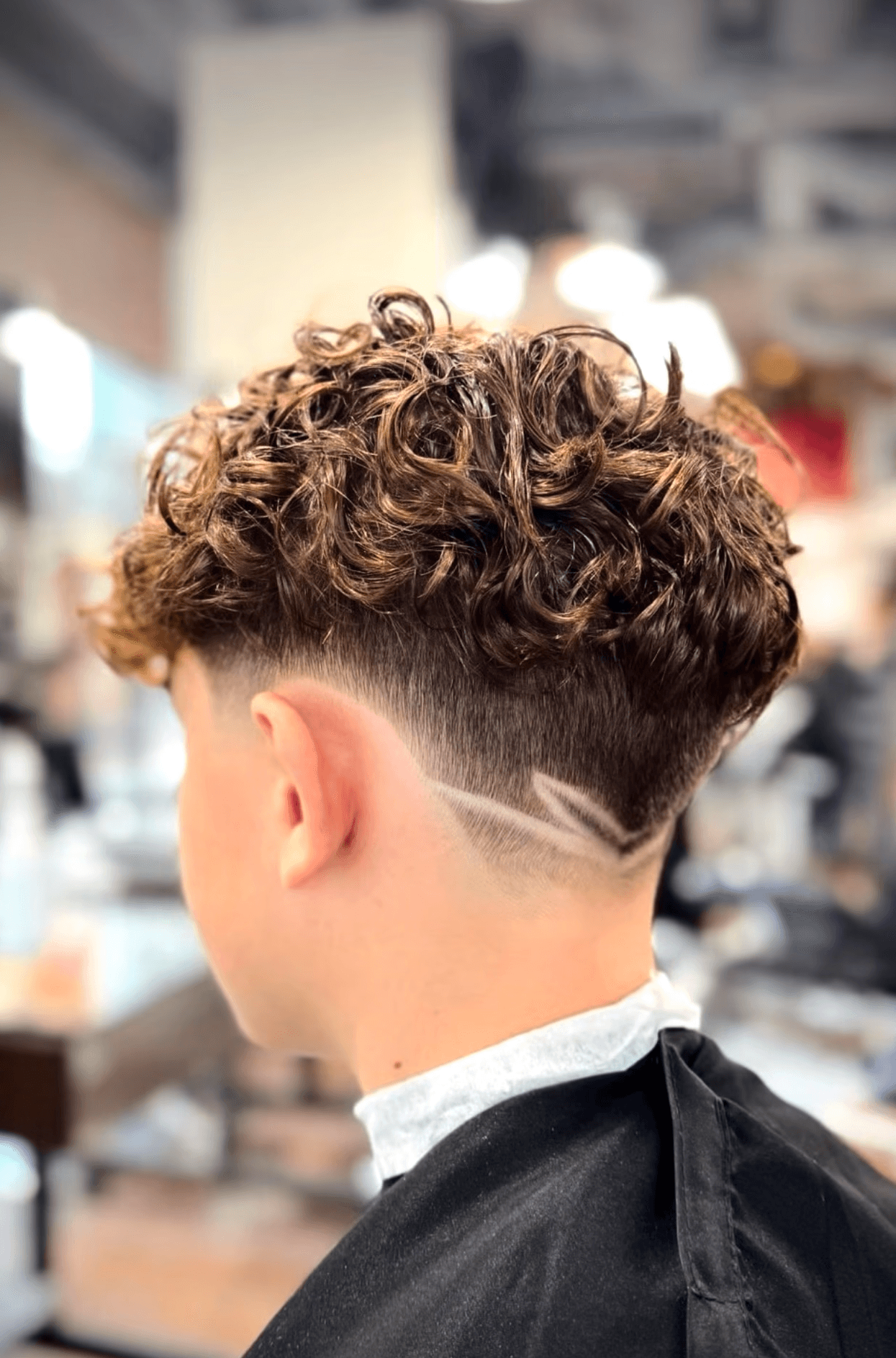 Youthful fade haircut featuring a custom part design, created by Courtney Palmore for a trendy and modern look.