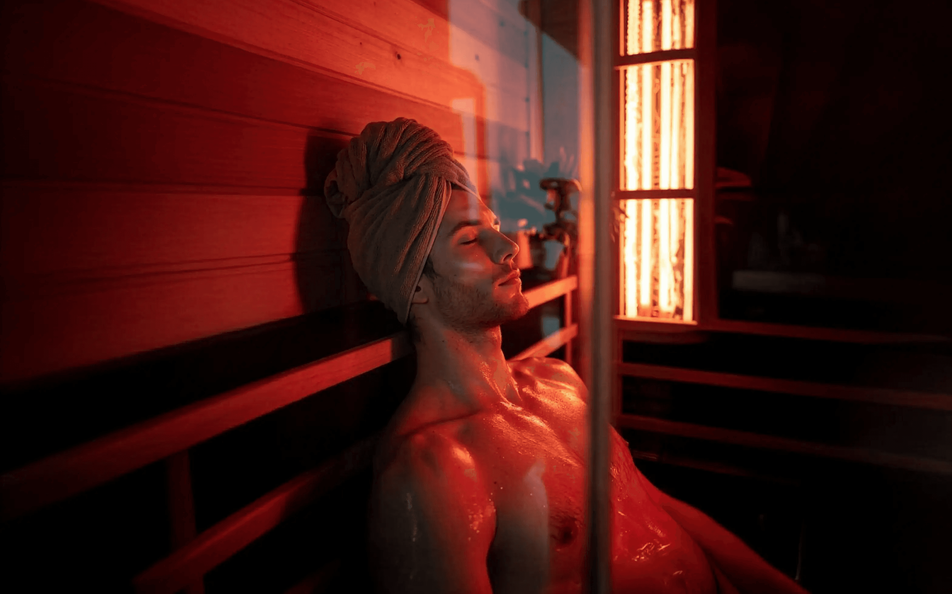 A man sitting in the sauna house with a towel on the head