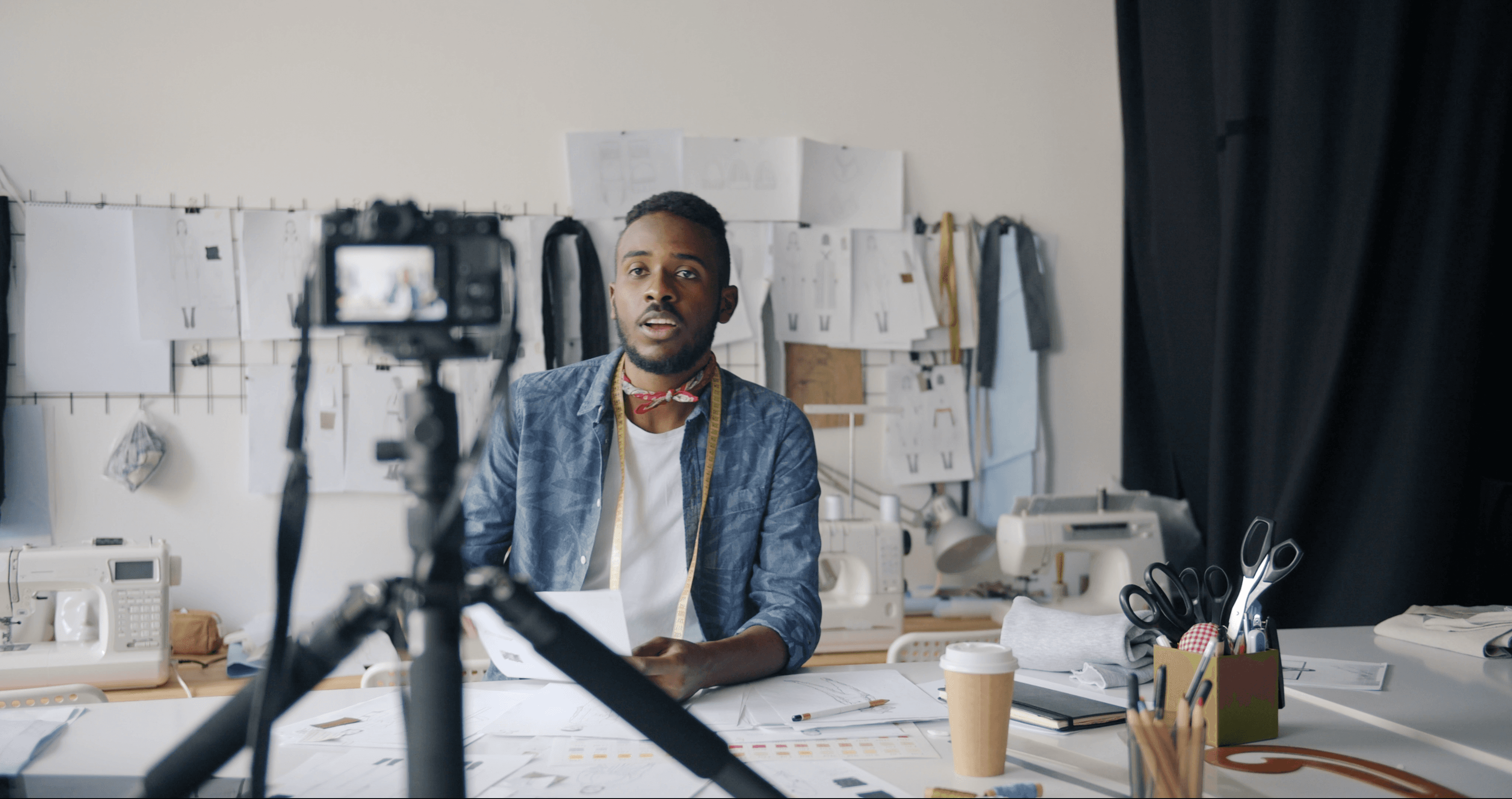 Independent fashion creator building their media brand on Playhuman — filming at a design studio desk with garment sketches