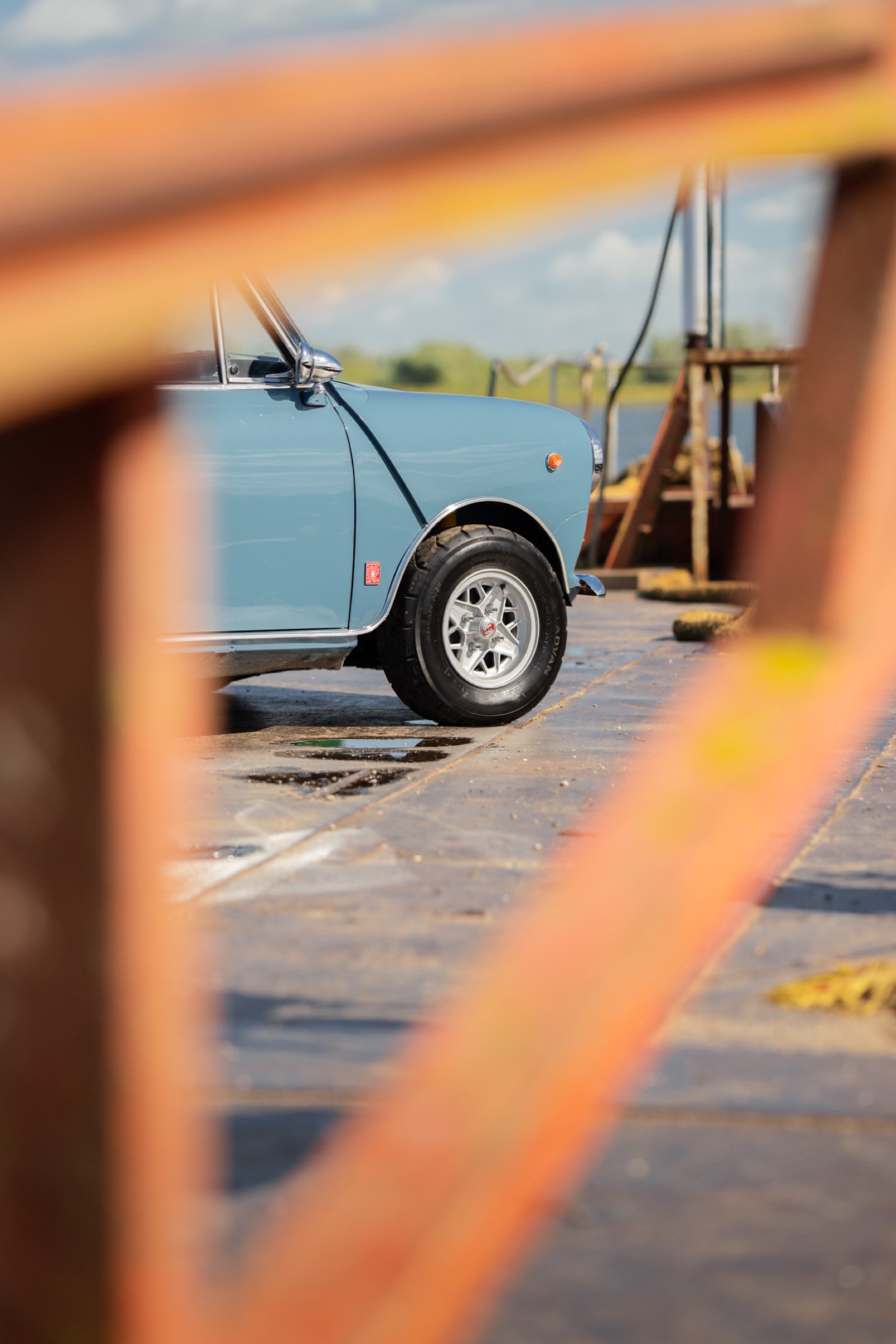 A trailer sits on a dock, framed by wooden railing, with calm water and a distant shoreline in the background.