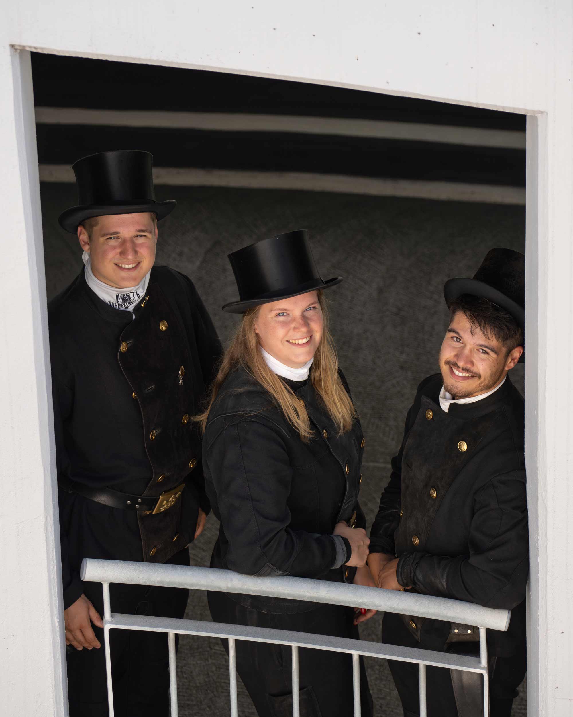 Three people in traditional attire and top hats smiling, representing storytelling for Zentralverband-Deutscher-Schornsteinfeger