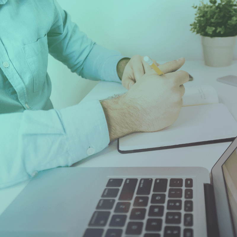 Man in a blue t-shirt smiling confidently while standing against a light wall in sunlight