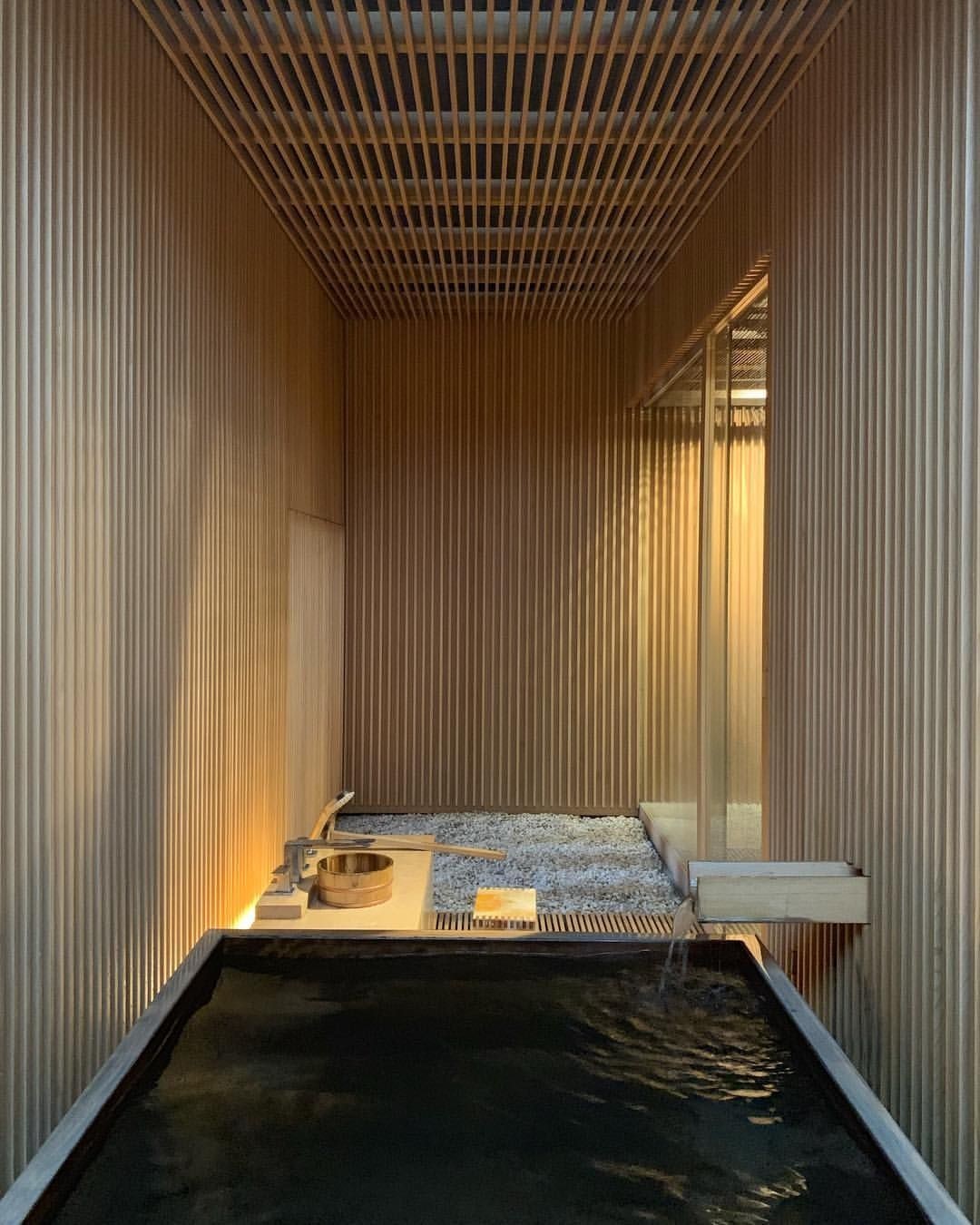 Dark tiled bathing room with a deep soaking pool, wooden bench, and a bar of soap on a tray.