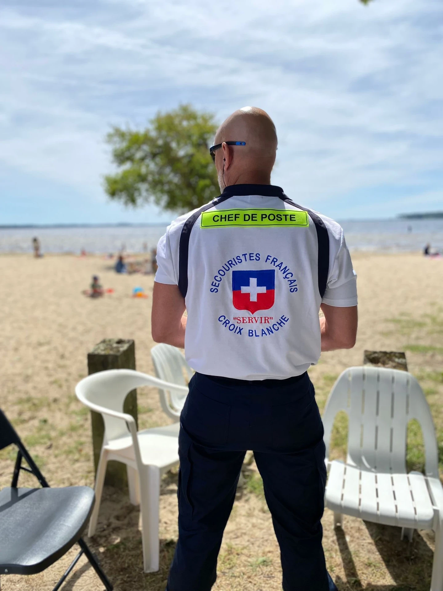 Secouriste français sur une plage, en uniforme Croix Blanche, près de chaises vides.