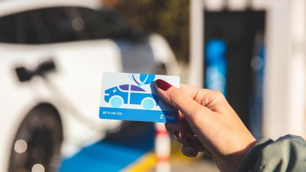 Person holding a Z Volt charging card in front of an electric vehicle charging station, highlighting Zurich's launch of the Z Volt charging service with a unified price model for electric vehicle users