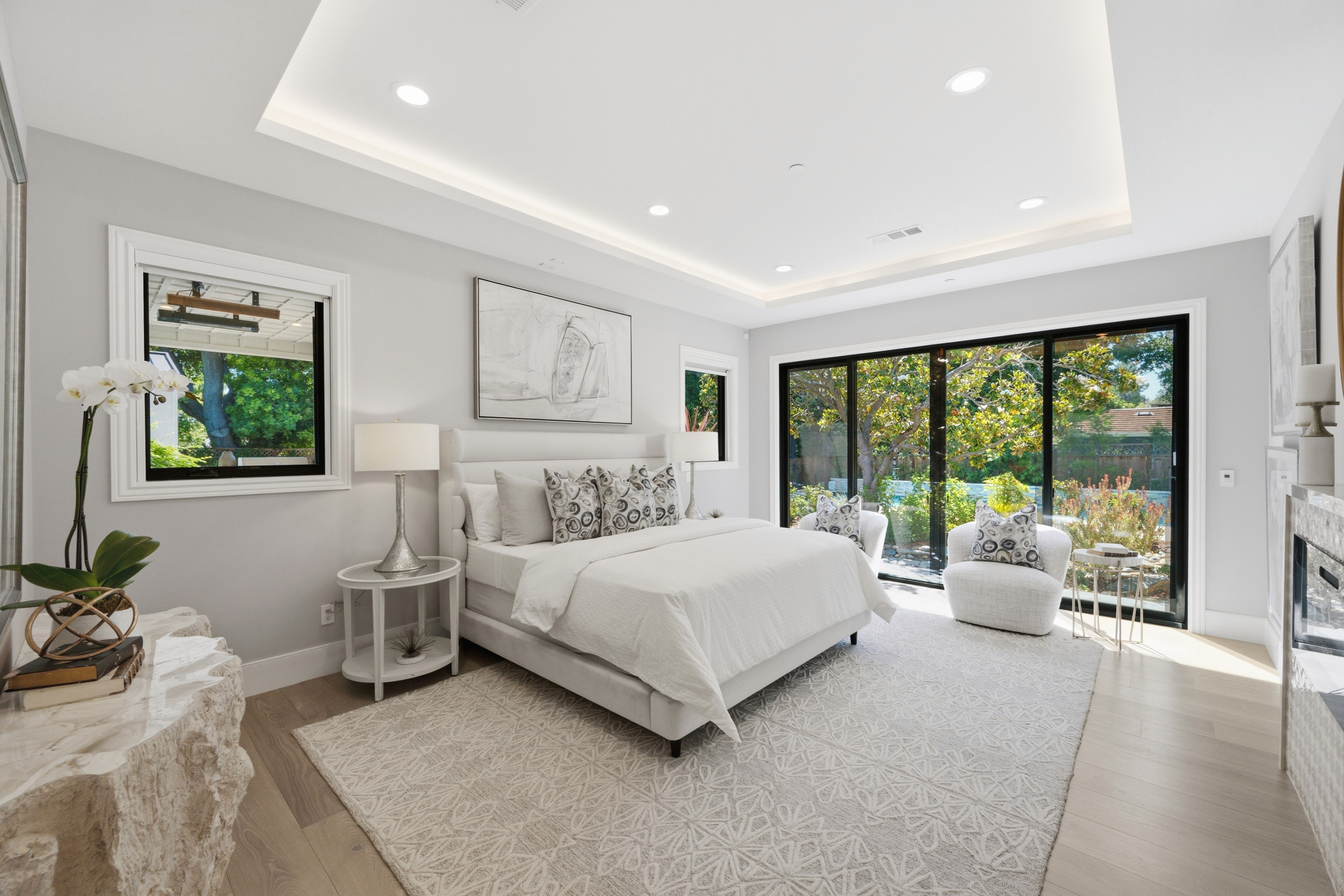 Primary bedroom with a tray ceiling, upholstered bed, and sliding glass doors to the backyard.