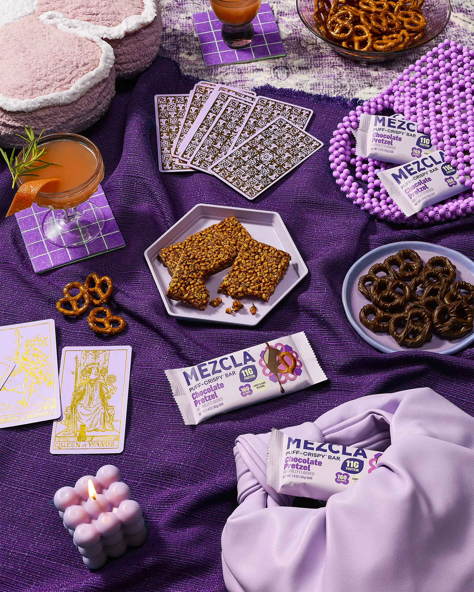 Mezcla Chocolate Pretzel protein bars on purple fabric with pretzels, tarot cards, a cocktail and a lit candle