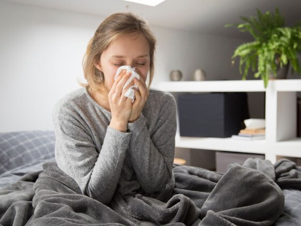 A woman blowing her nose on a bed.