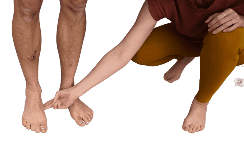 Teacher in a squat reaching to tap the inner arch of a standing student’s foot