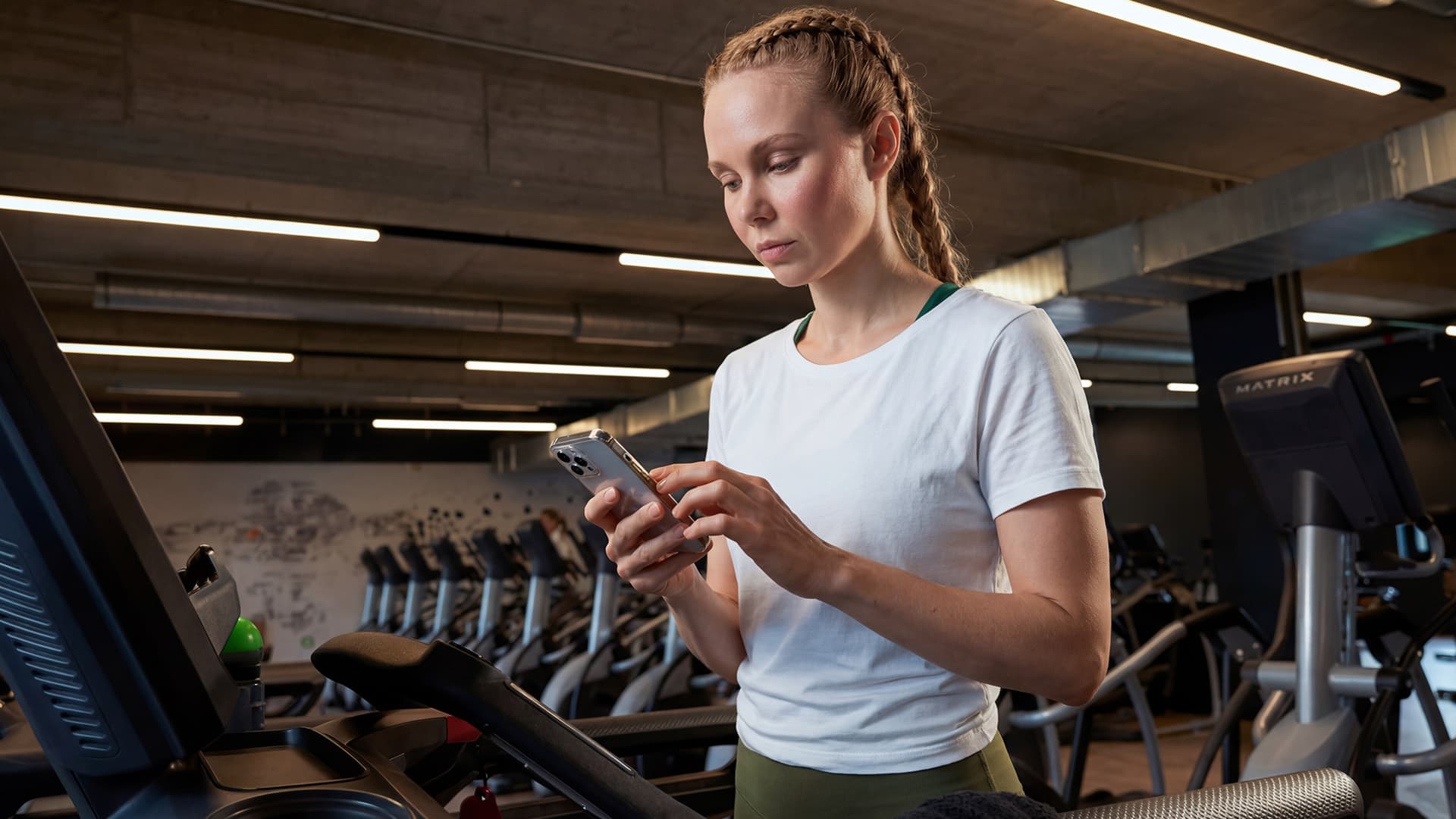 Frau schaut auf ihr Smartphone am Laufband und dokumentiert ihr Training im Fitnessstudio