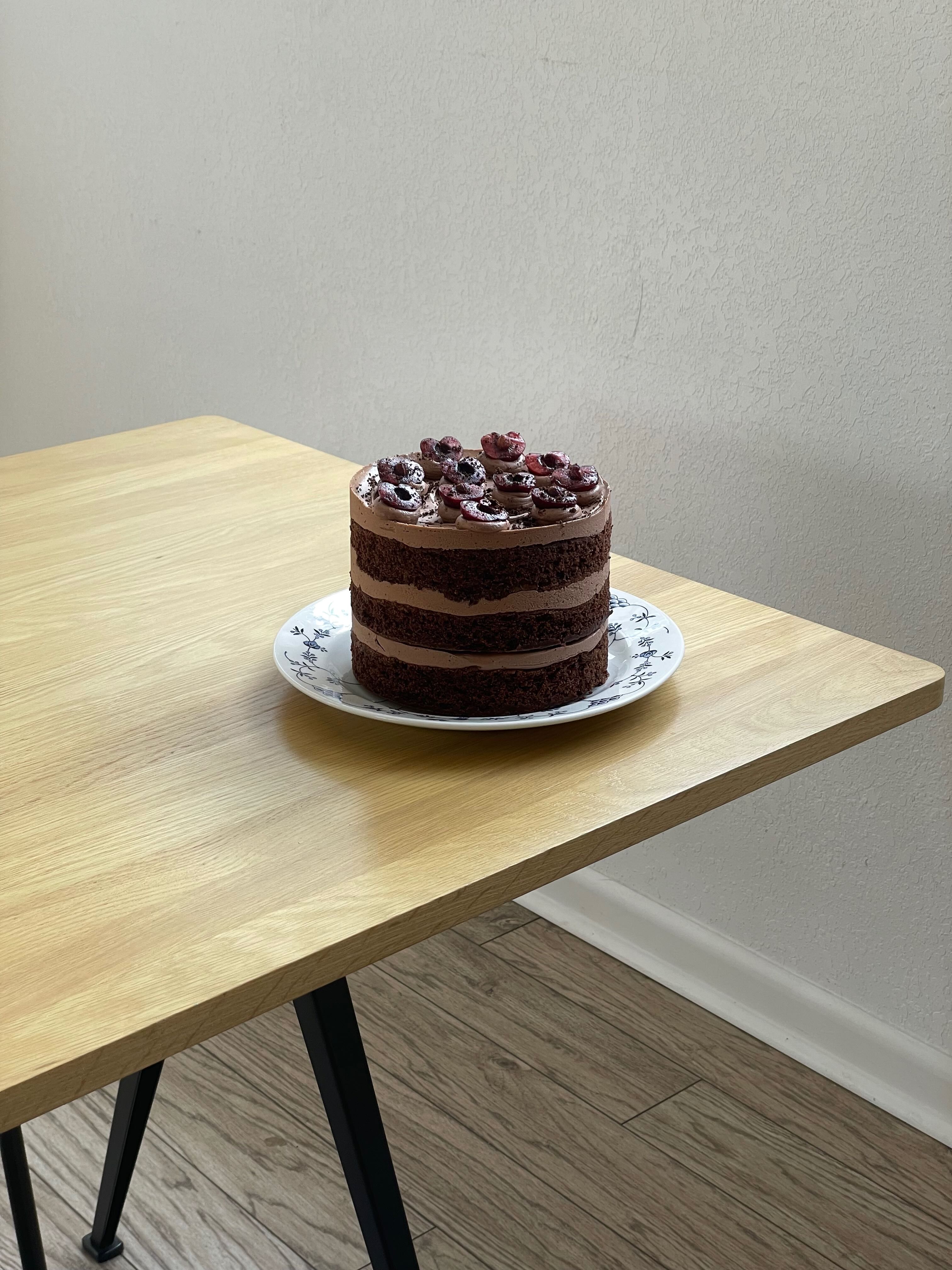 Cozy cafe corner with a round terrazzo table surrounded by wooden chairs, decorated with potted plants and a large mirror reflecting warm light.