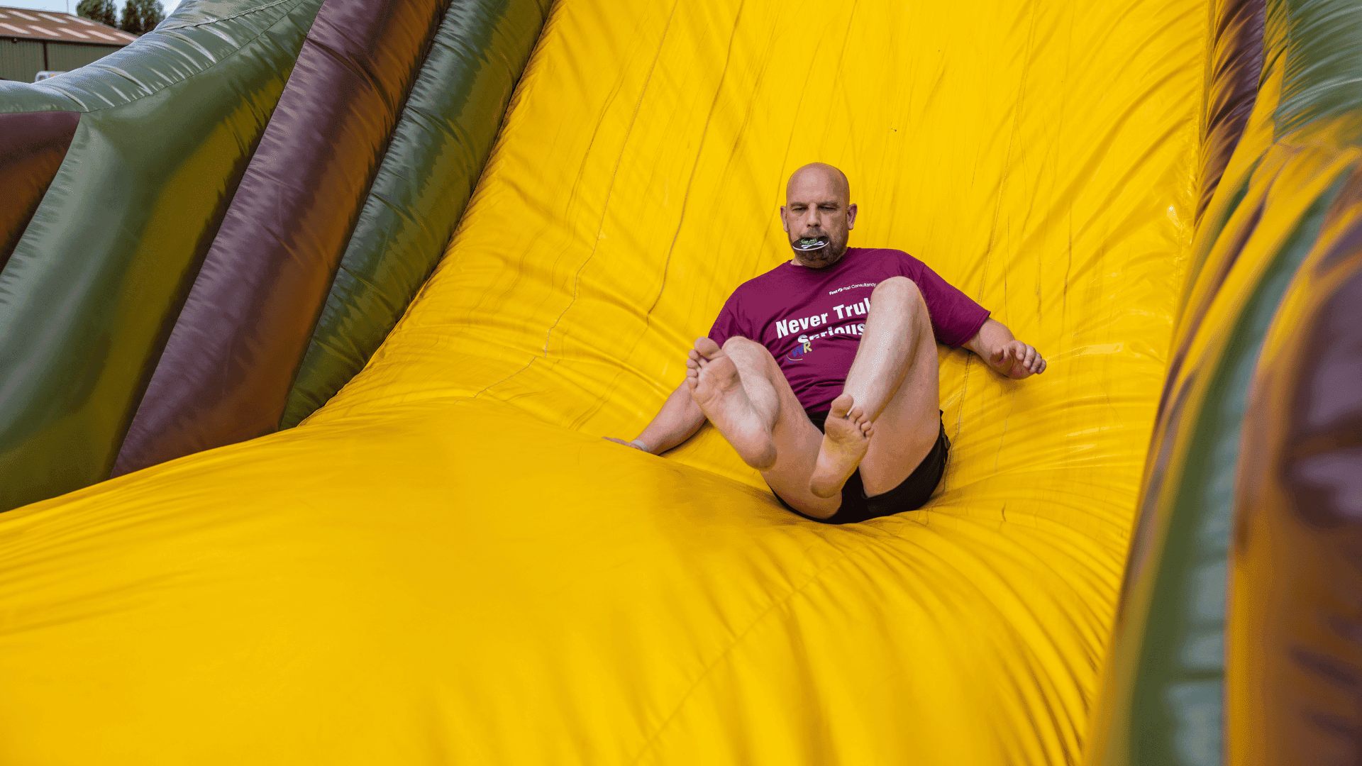 Outdoor team-building event with participants wearing matching blue shirts, taking part in inflatable obstacle courses and games, smiling and cheering, with the words 'ENTER A TEAM' in large bold white and green text across the image.