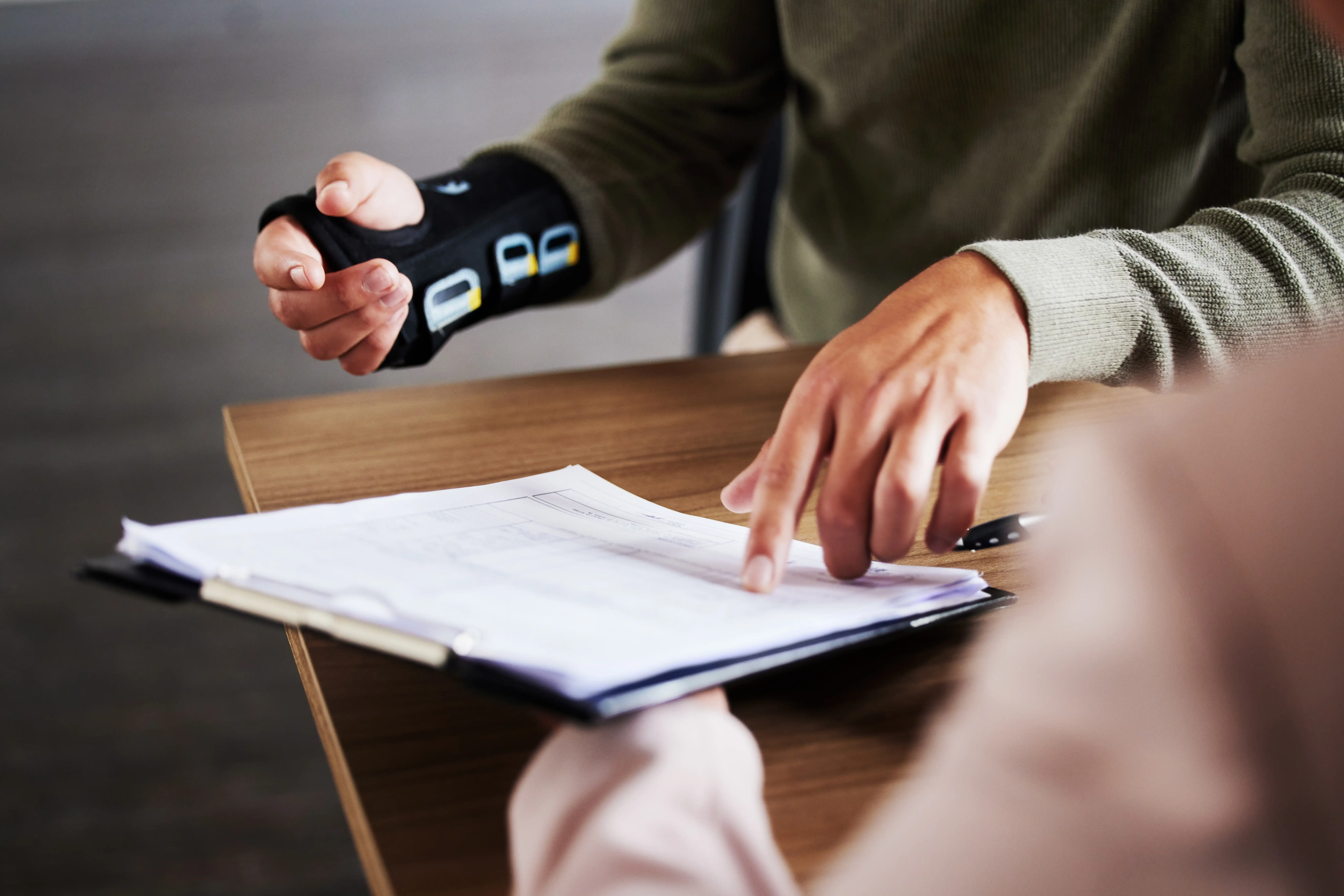 Close-up of an employee wearing a wrist brace reviewing a job description document with a manager, illustrating the evaluation of essential vs. marginal job duties under California disability law
