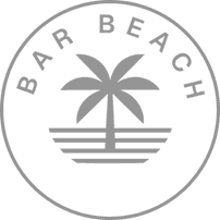 Smiling man with short hair and beard wearing a beige shirt stands against a softly lit gray background, casting gentle shadows. The mood is warm and joyful.