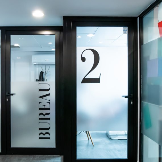 Couloir de bureaux avec des portes en verre dépoli portant les inscriptions « BUREAU » et « 2 ». Design moderne et épuré, avec des tons neutres et un éclairage tamisé, créant une atmosphère professionnelle.