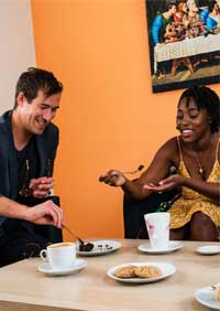 Two friends sharing dessert with tea and coffee at a cozy café table.