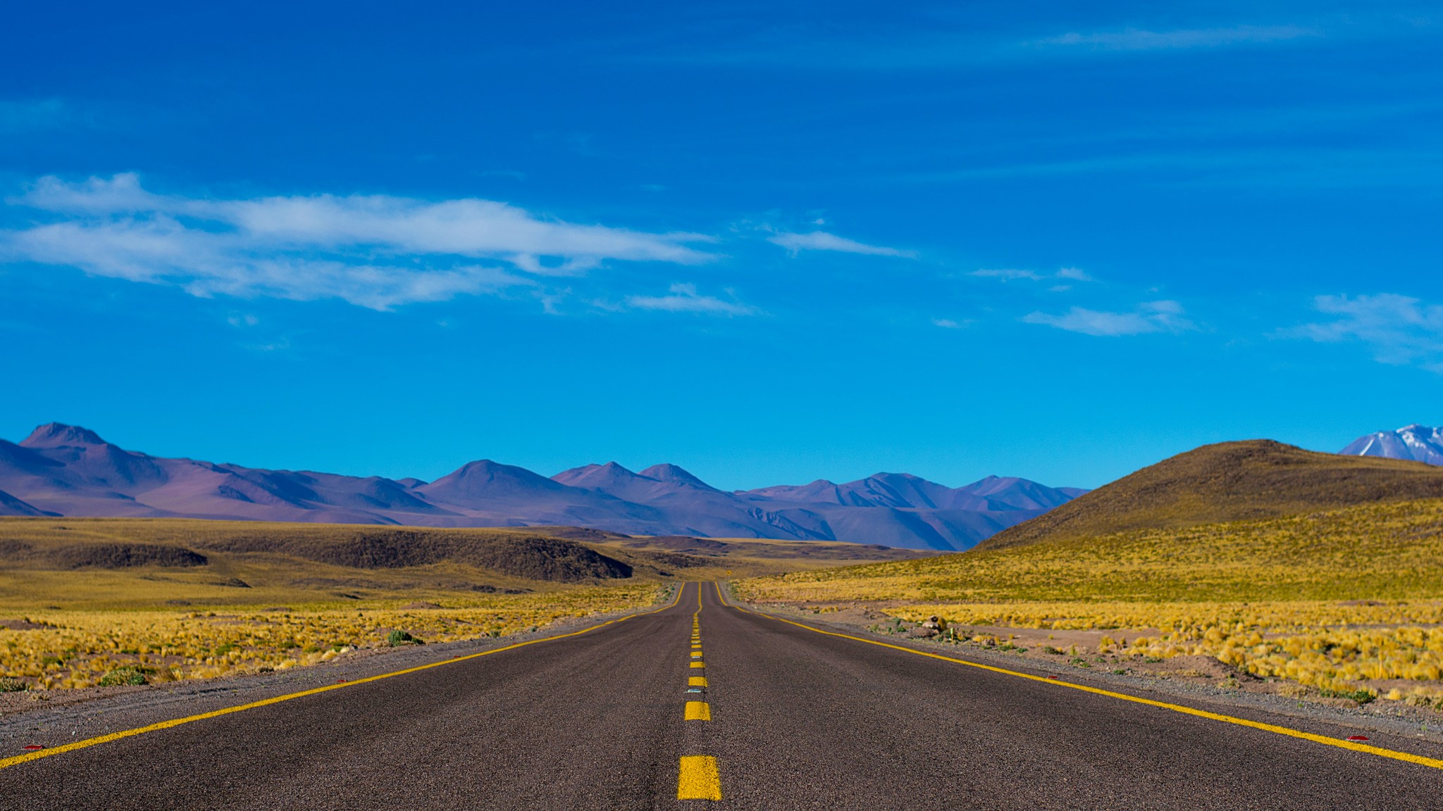 Image looking down a long striaght road with a nice scenery with hills in the background