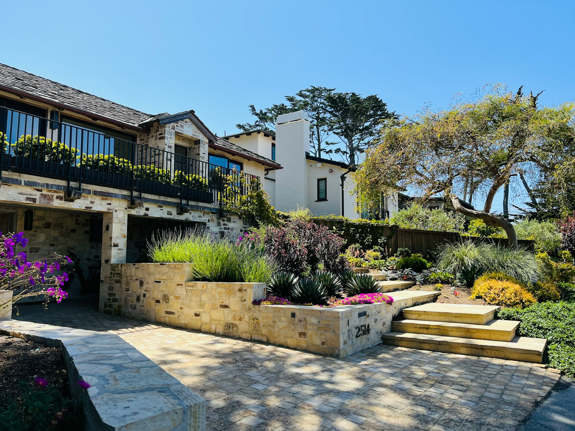 Illustrative upscale coastal-style home with stone walls, a landscaped courtyard, and mature trees; not a listing.