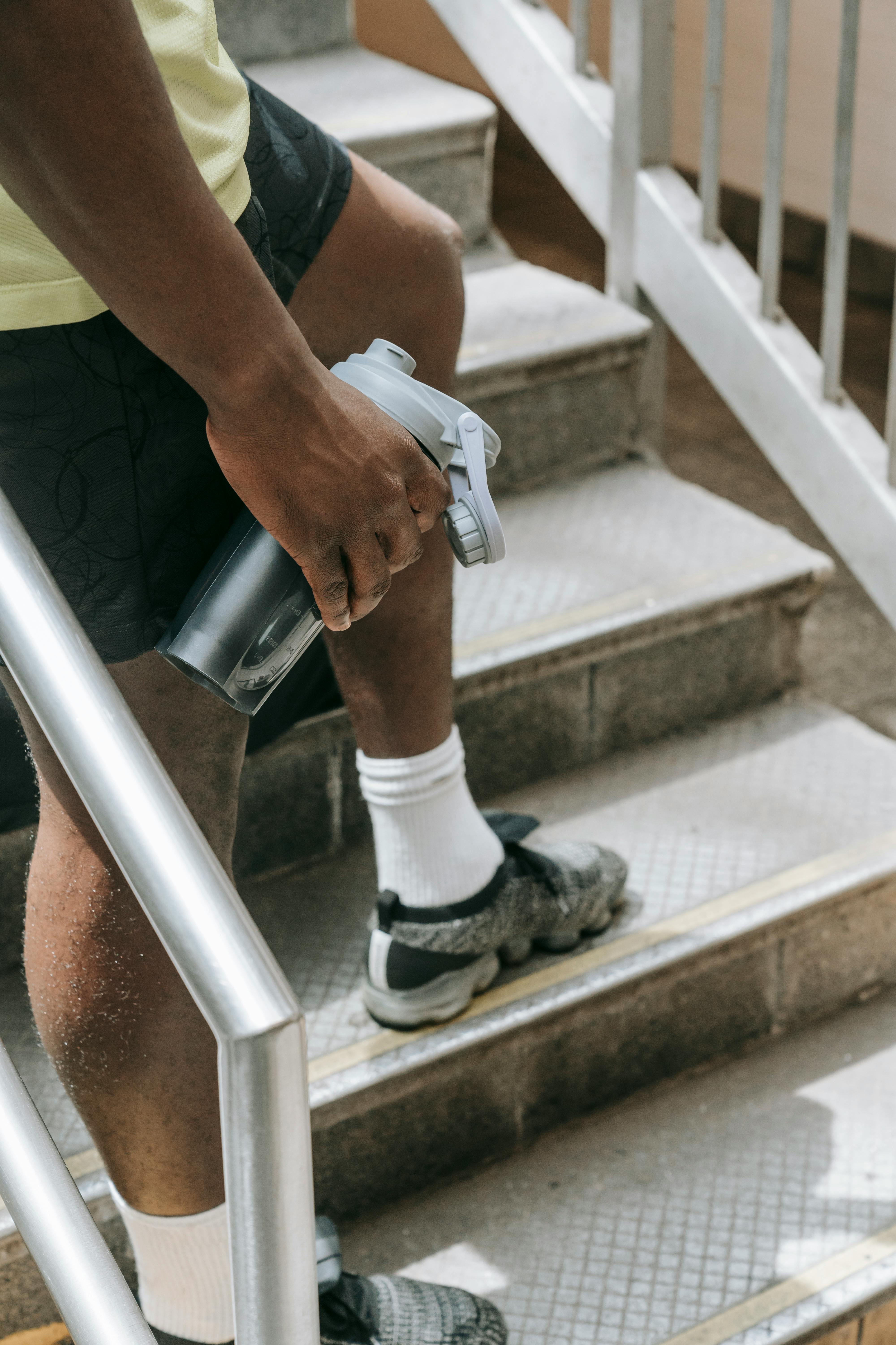 Man in sports clothes, standing on outdoor staircase holding water bottle