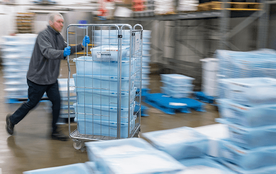 Mitarbeiter schiebt einen Gitterwagen mit gestapelten Mehrweg-Fischkisten durch das Lager von Deutsche See – nachhaltiges Logistik- und Verpackungsdesign.