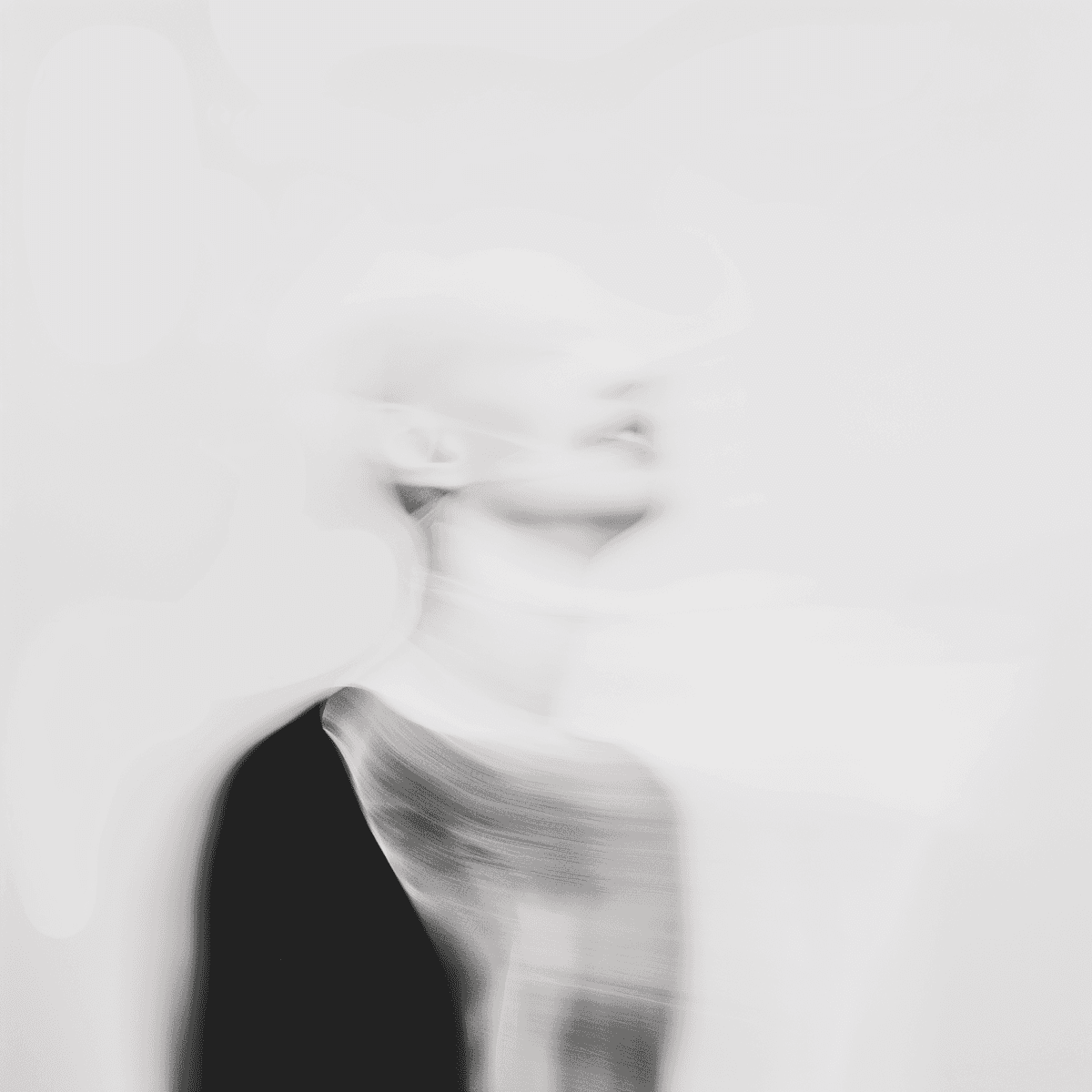 Abstract blurred image of a person with a ghostly appearance, wearing dark clothing against a light, ethereal background.