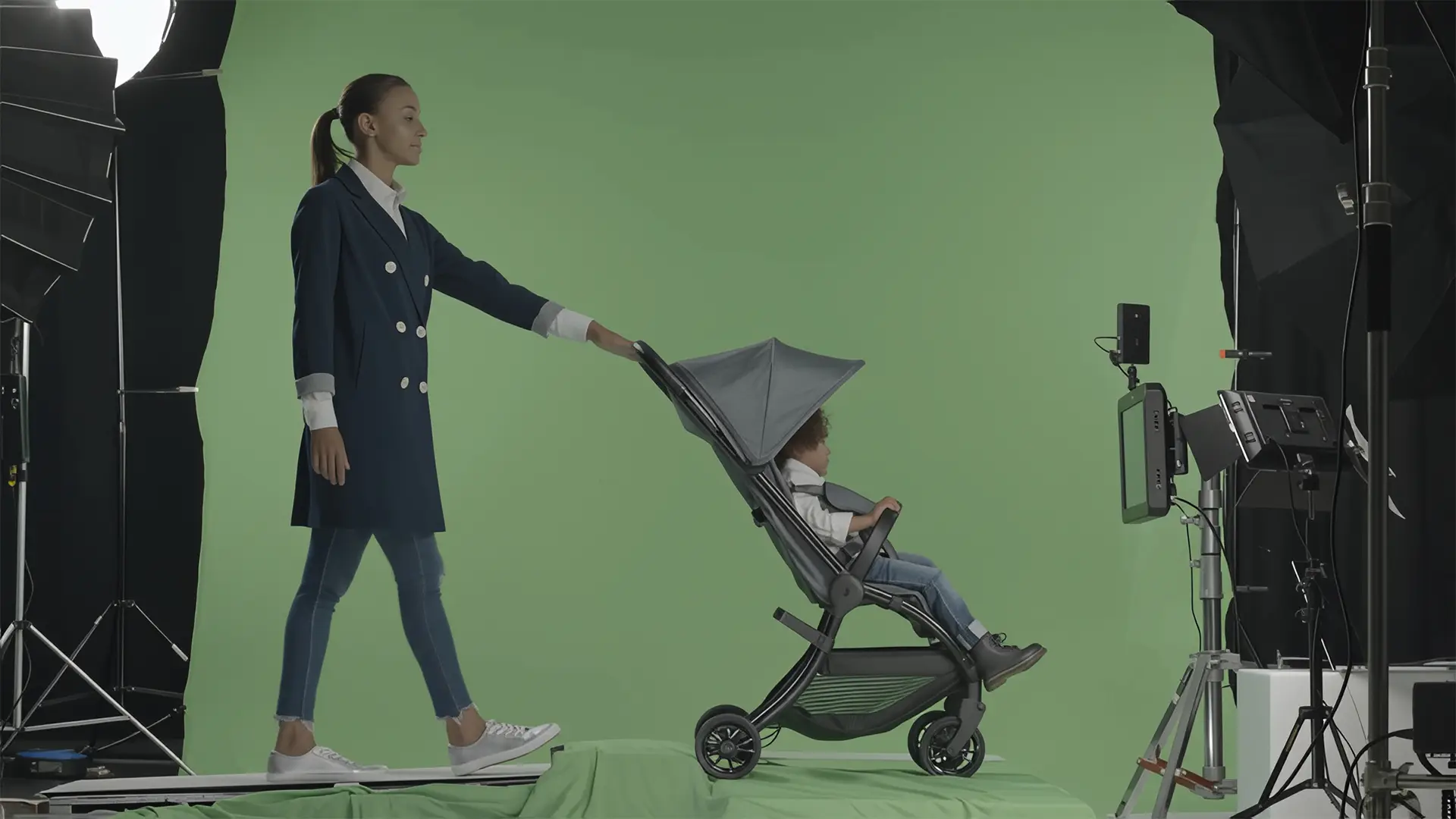 Woman pushing a JUNIORJONES stroller in a studio setup with green screen and lighting equipment visible.