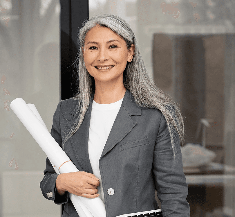 Smiling woman with long gray hair holds rolled blueprints and a solar panel. She's wearing a gray suit, conveying professionalism and eco-focus.