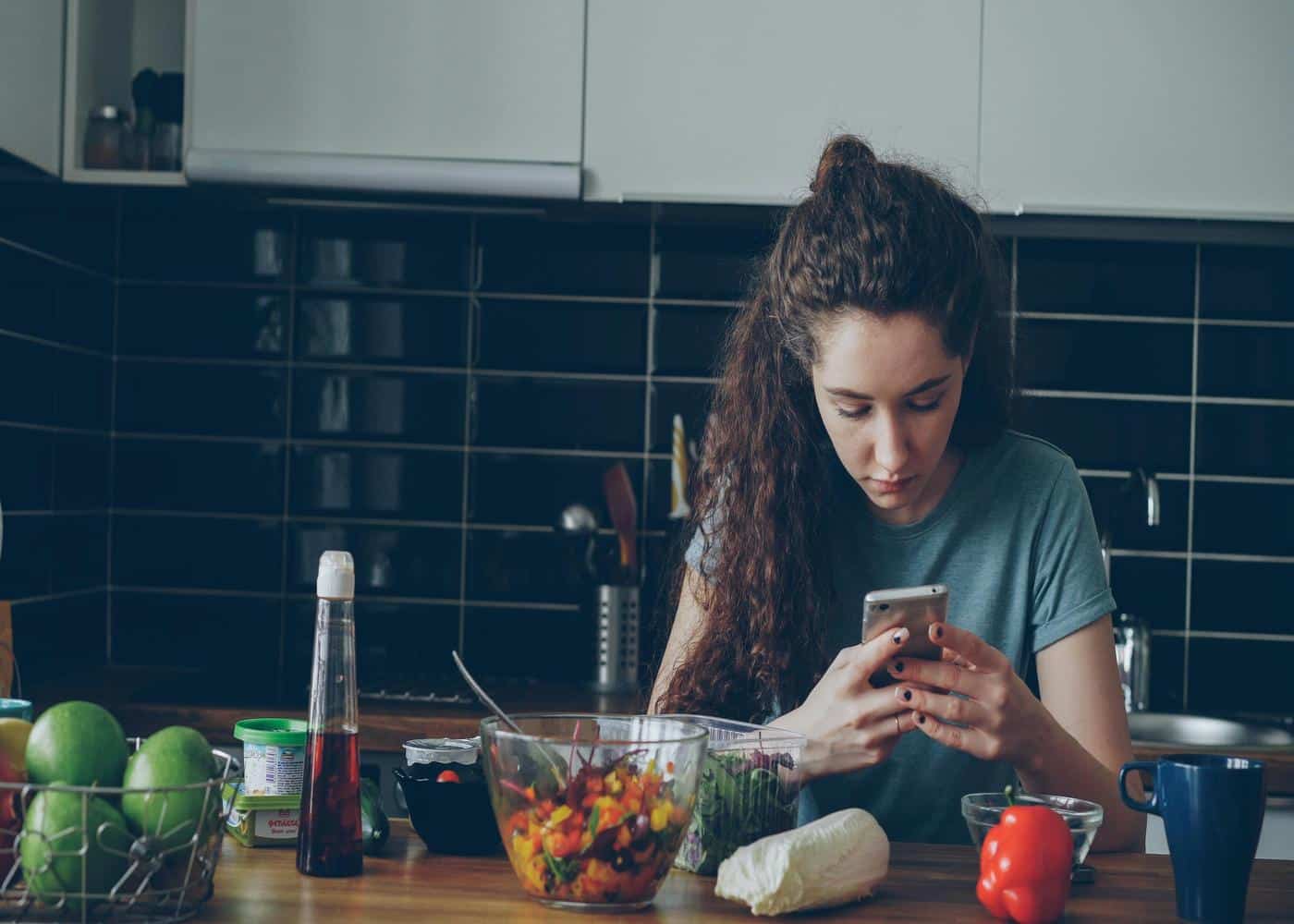 Woman with salad and veggies in front of her looking at smartphone