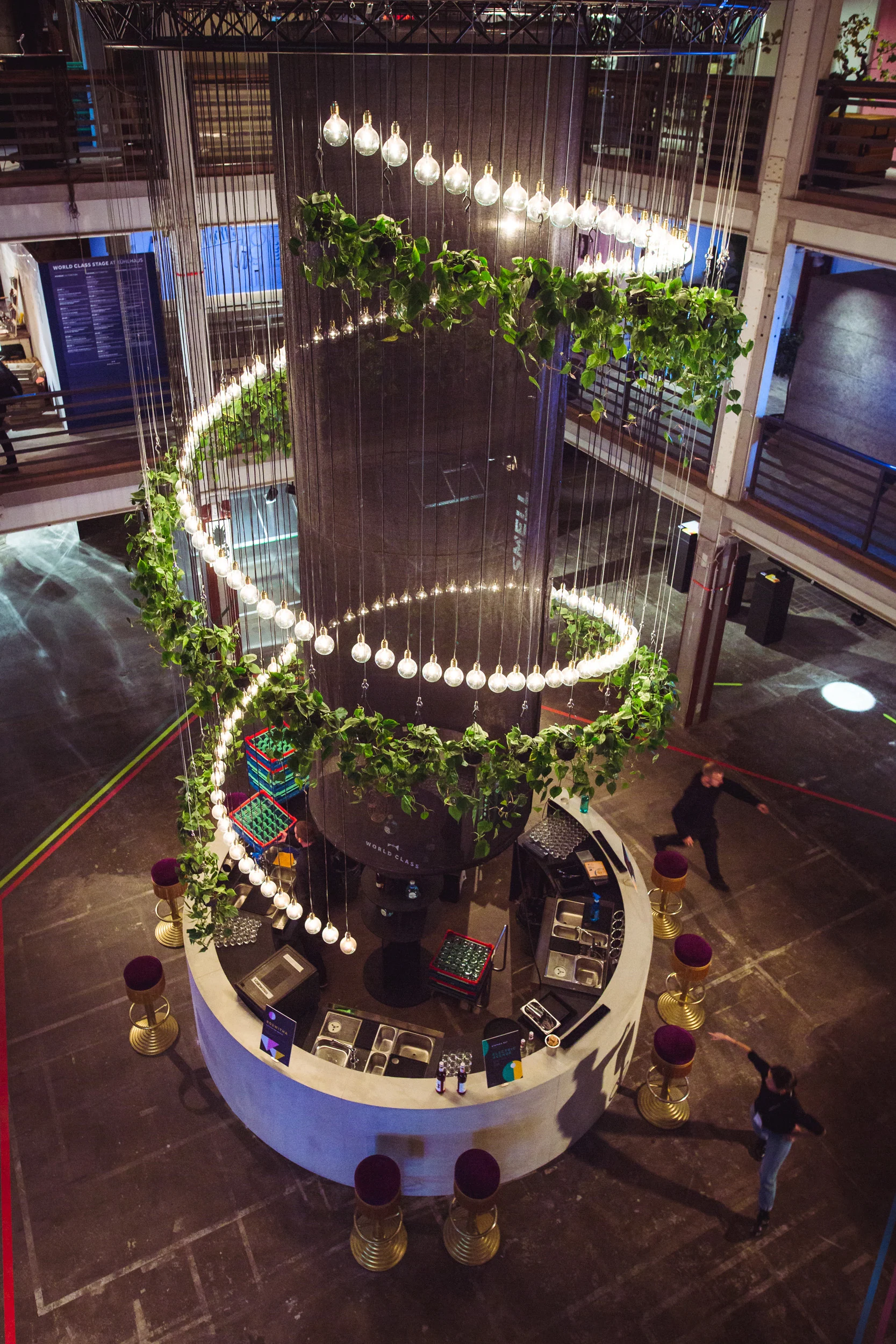 Bird's-eye view of the circular central bar at DIAGEO BCB18 with a tower wrapped in spiraling garlands of greenery and glowing bulbs.