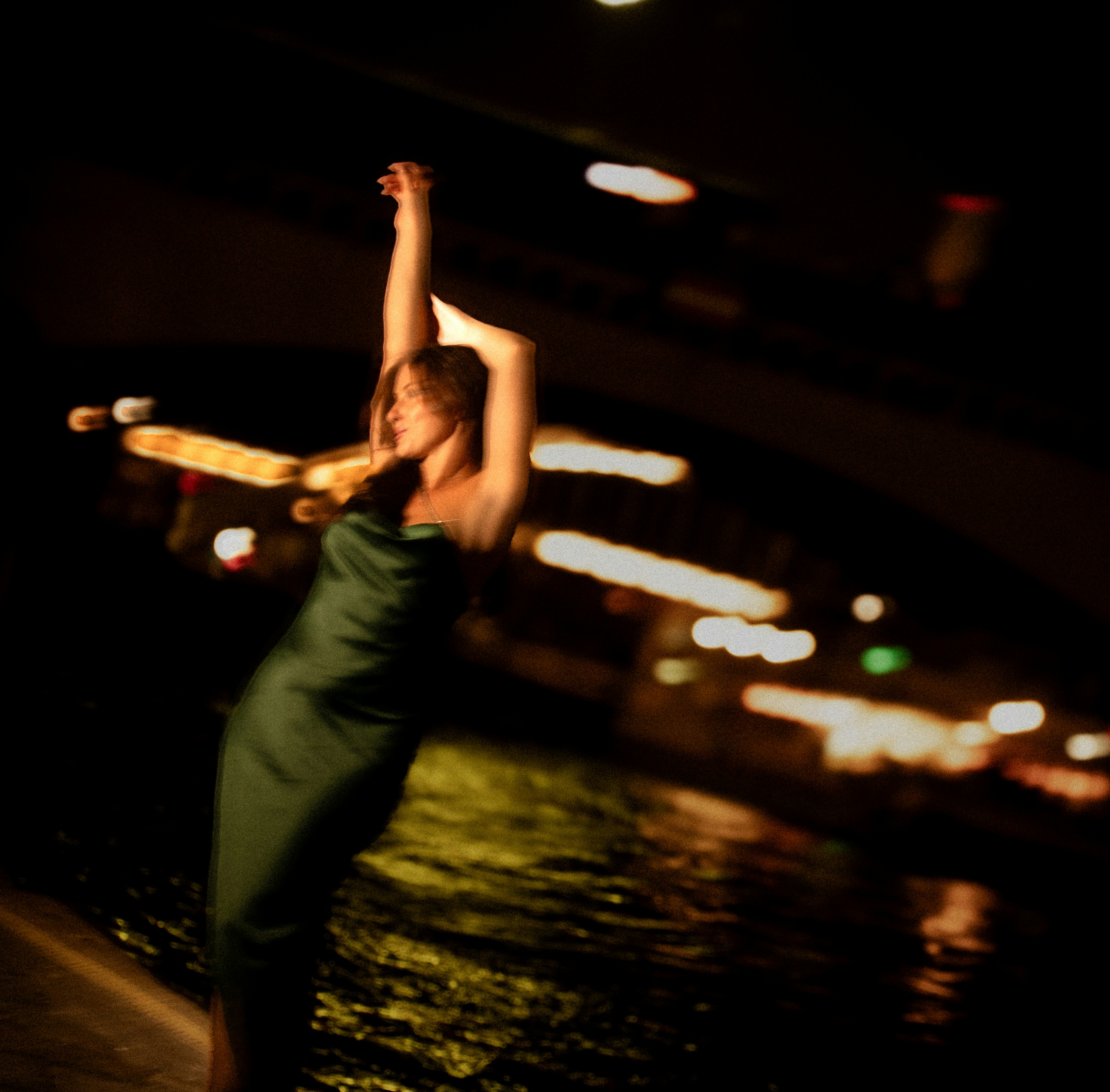 Woman in a green dress dancing by the water at night.