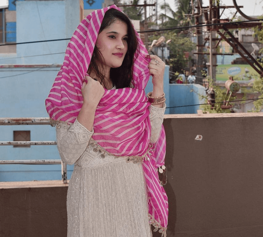 Smiling young man with short hair poses against a dark background, wearing a green button-up shirt.