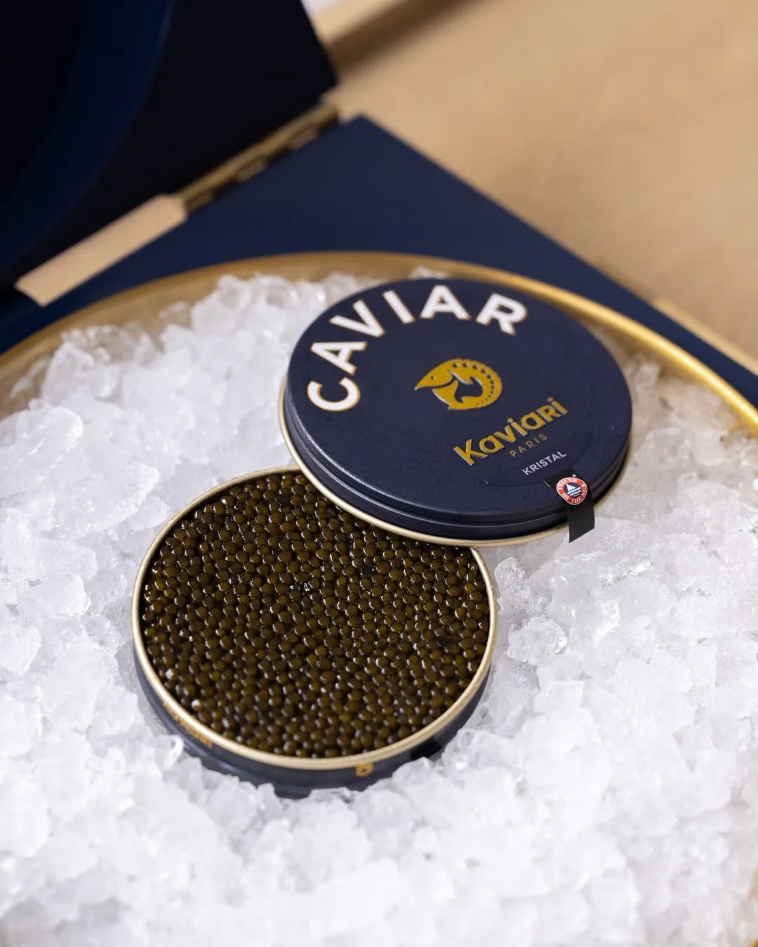 A tin of Kaviari caviar resting on a bed of ice, with the lid slightly open to reveal the shiny caviar pearls inside.