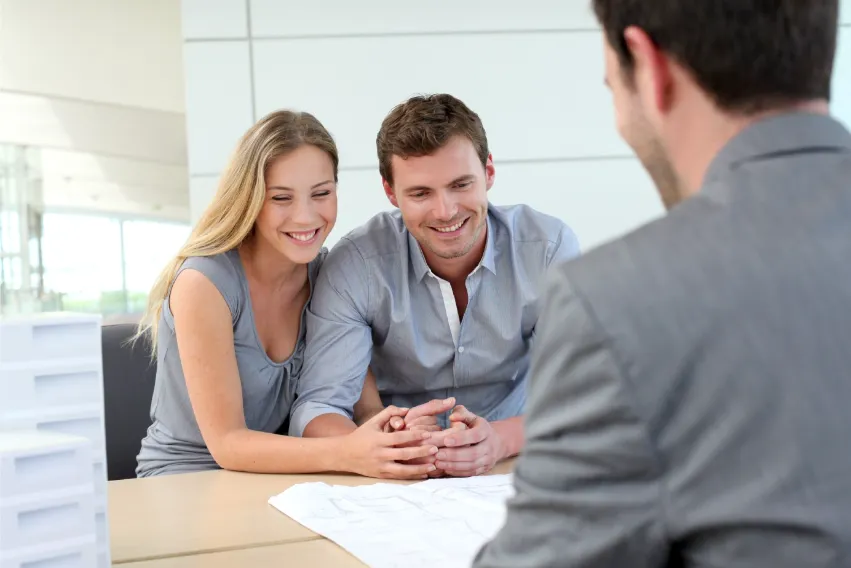 Couple smiling and meeting with financial advisor at desk with blueprints.