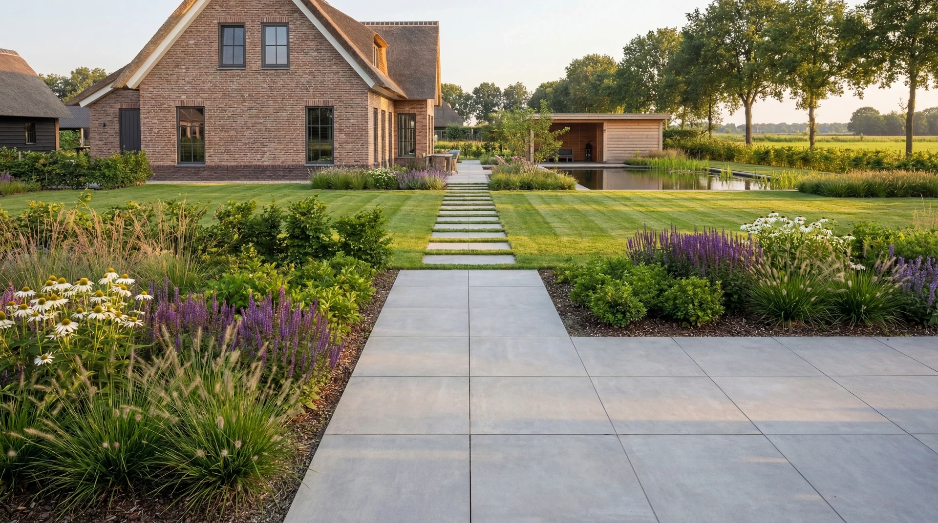 Modern bestrate tuin met groen en bloemen bij landelijk huis met rieten dak.