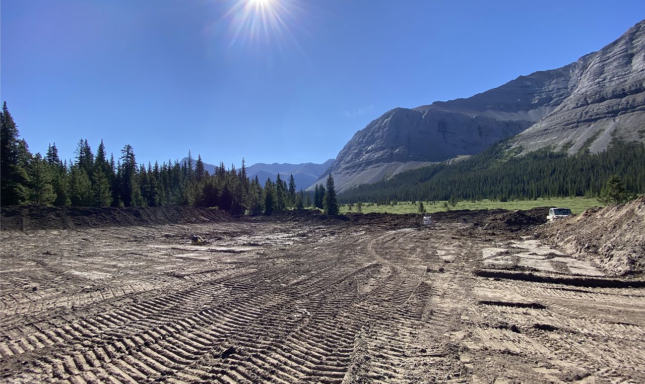 Trail refurbishment earthworks in progress at Cardinal River Headwaters with heavy equipment and Rocky Mountain backdrop