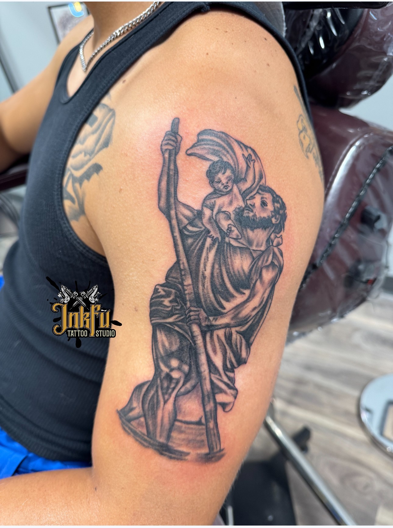 Black and grey religious figure tattoo on the upper arm, by Meer Rich