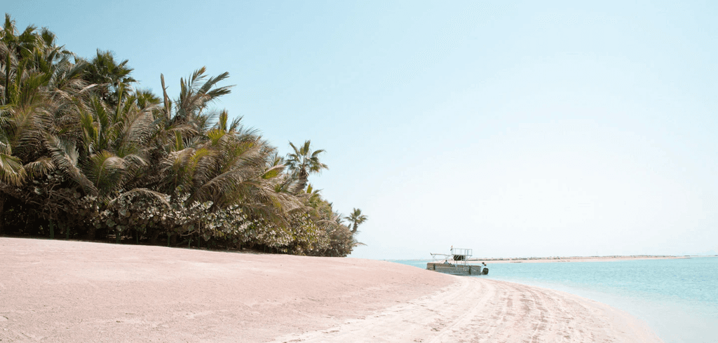 A boat rests on a sandy beach with palm trees in the background, set in The World Islands.