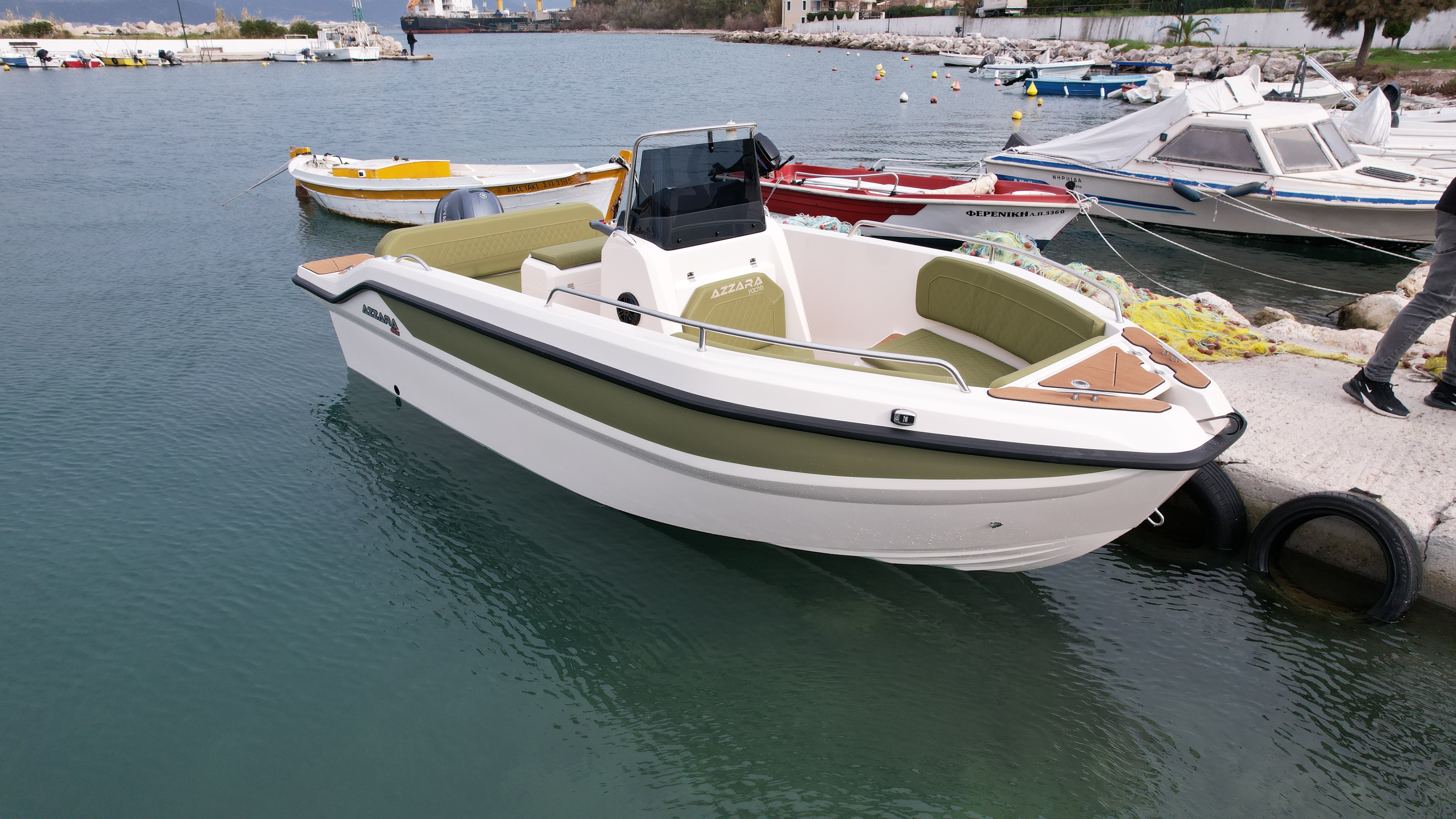 White Nireus Azzara Pnoe speedboat with green interior seating moored at a Mediterranean harbor dock alongside other boats.