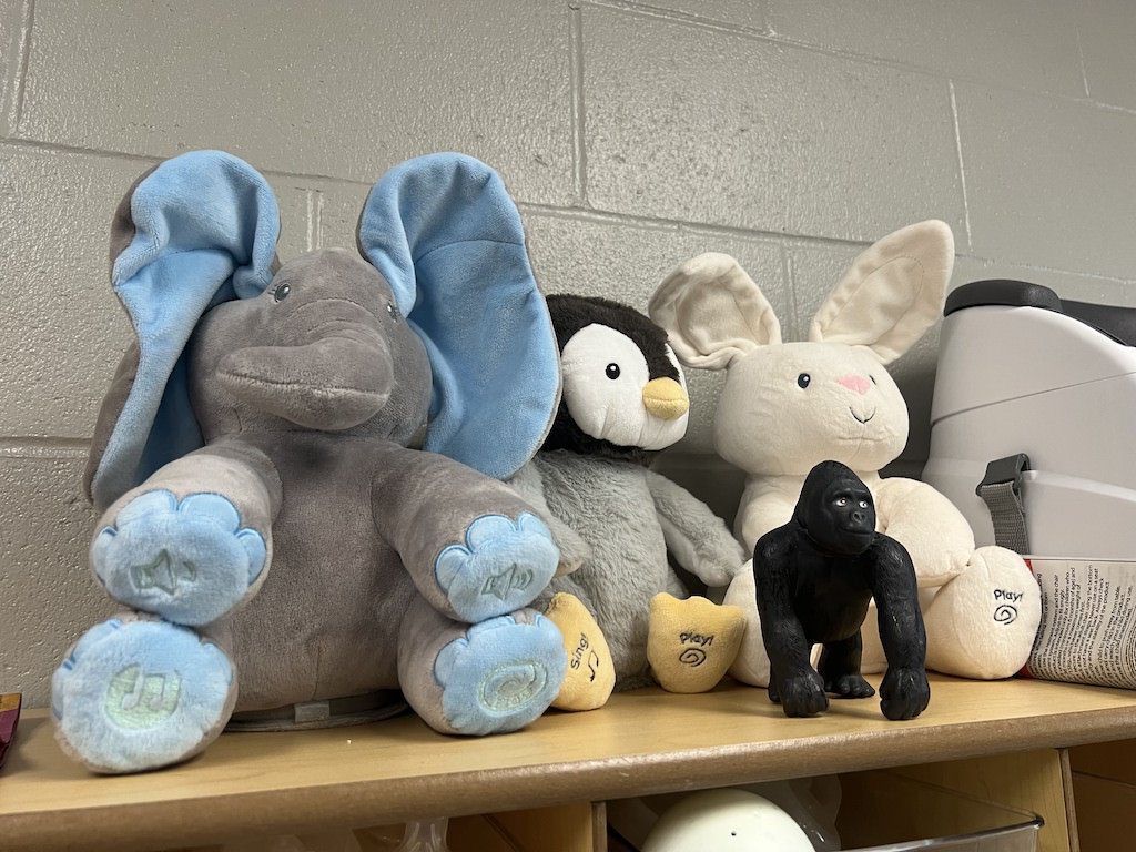 Stuffed animals and a small gorilla figurine sit on a top shelf above the area where moms store their diaper bags.